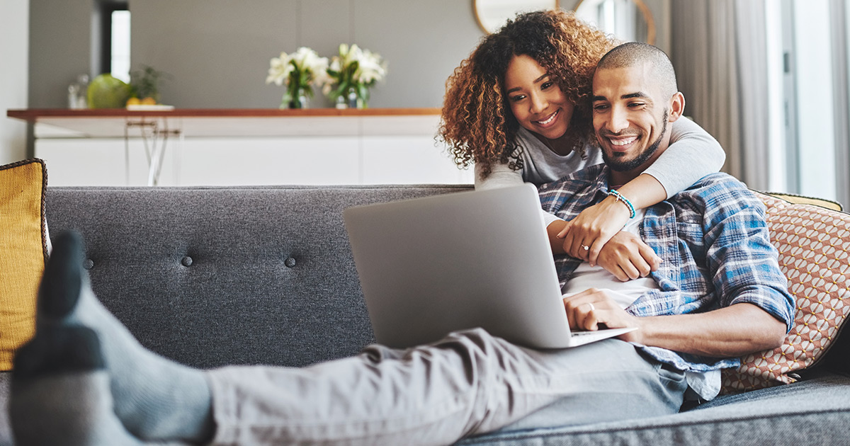 Man and woman sitting on couch smiling looking at a laptop