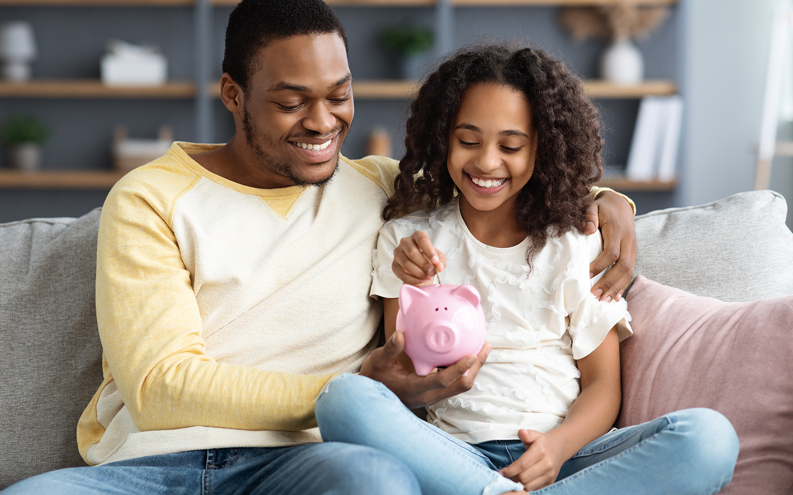 Dad and daughter looking and smiling at a piggy bank
