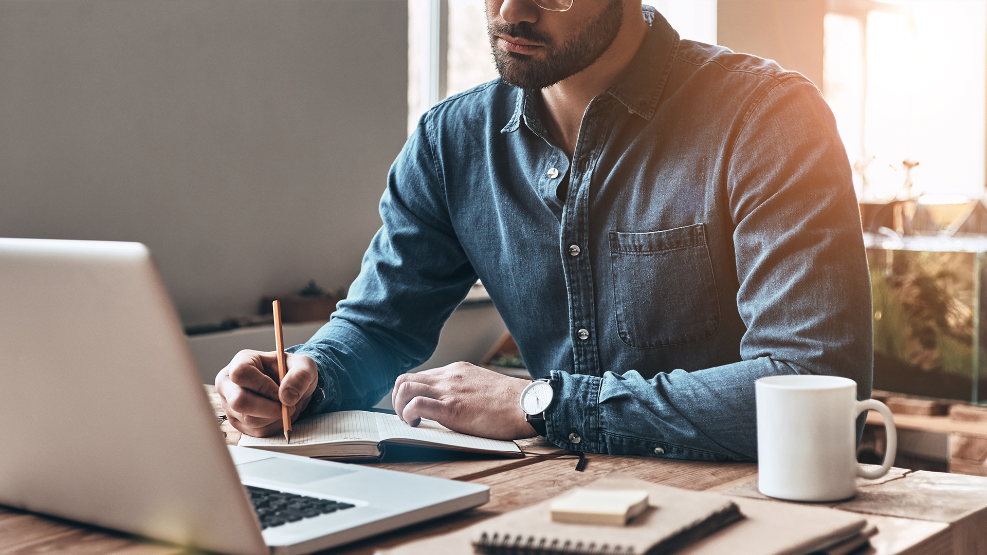 man working on his laptop and taking notes on desk