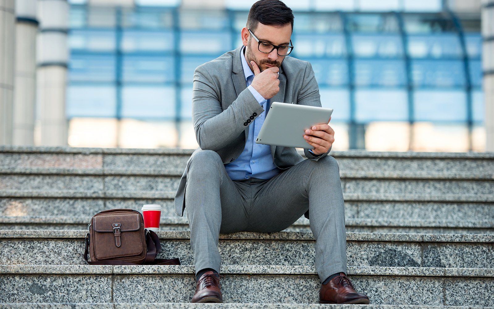 Business man in grey suit sitting on the staircase looking at a tablet