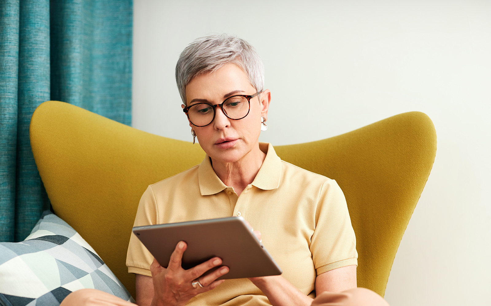 Mature woman sitting at home on armchair using digital tablet