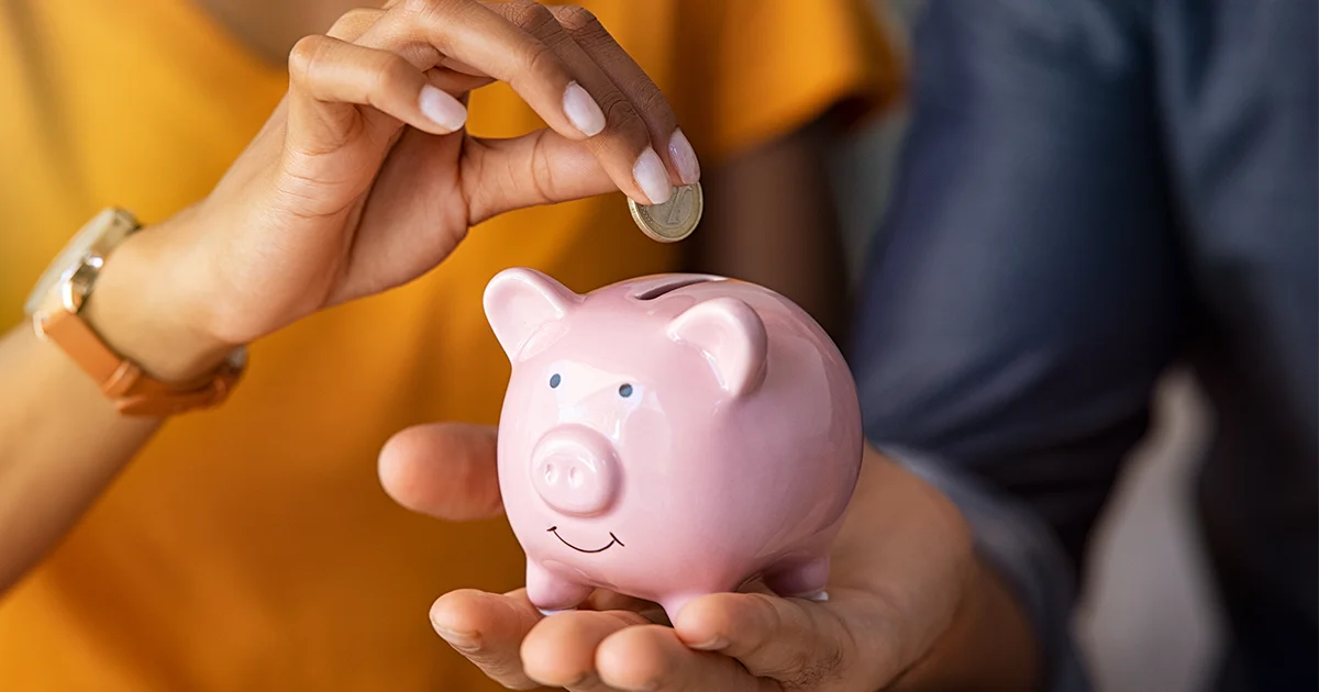 Close up of man holding pink piggybank while woman putting coin in it