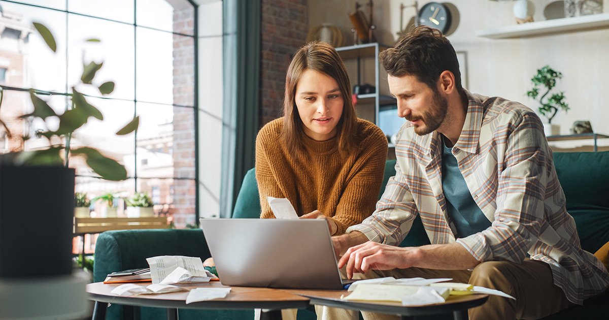  Couple utilisant un ordinateur portable sur un canapé d'appartement vérifiant les factures