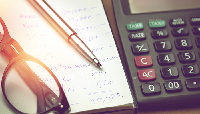 Glasses on a pad of paper with calculations. A pen sits on the pad of paper and there is a calculator on the side