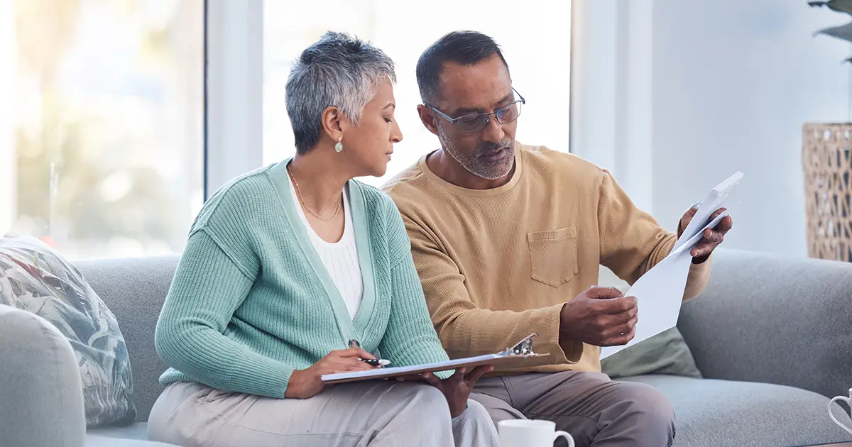 Finance documents and senior couple on sofa with bills