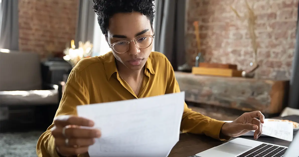 Focused young woman in eyeglasses looking through paper documents managing business affairs