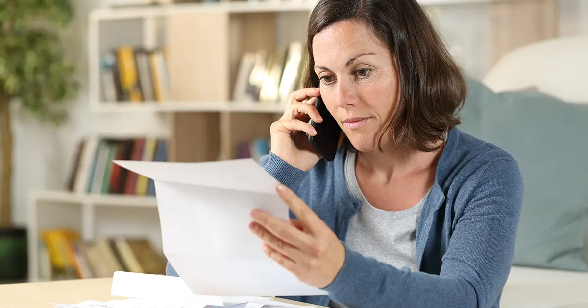 Serious adult woman checking letter calling on smart phone sitting in the livingroom at home