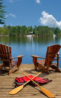 Two Adirondack chairs sit on a wooden dock overlooking the blue waters of a lake in Muskoka Ontario