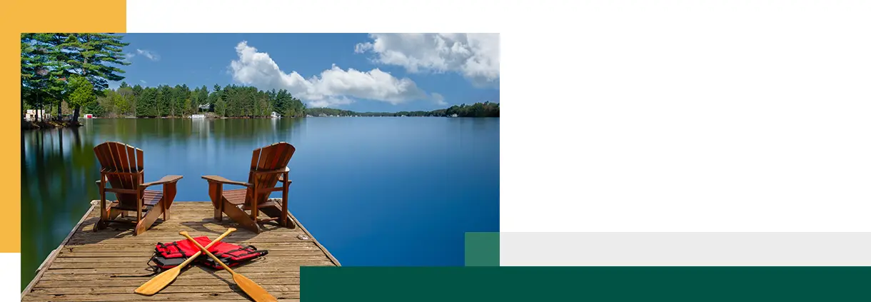 Two Adirondack chairs sit on a wooden dock overlooking the blue waters of a lake in Muskoka Ontario