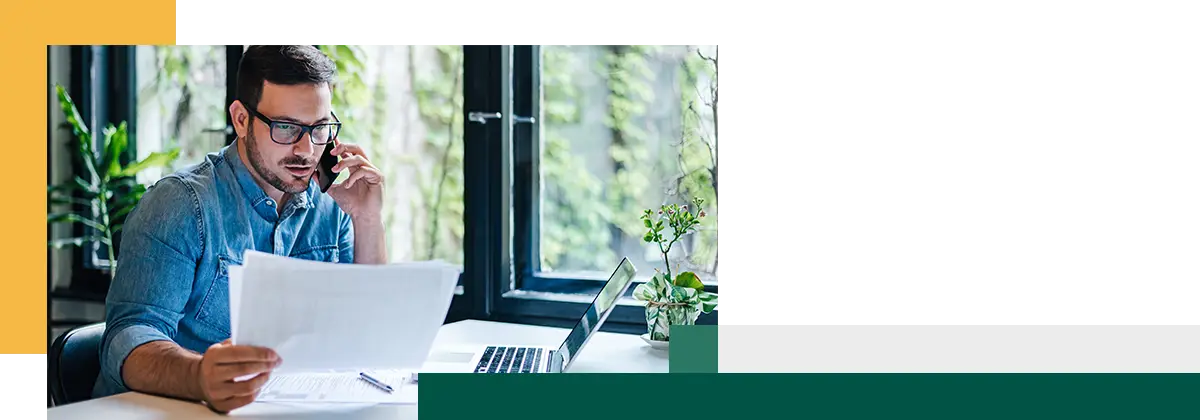 Portrait of young male working remotely holding paper and reading financial document