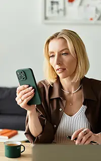 Woman in casual attire sits at home focusing on her phone