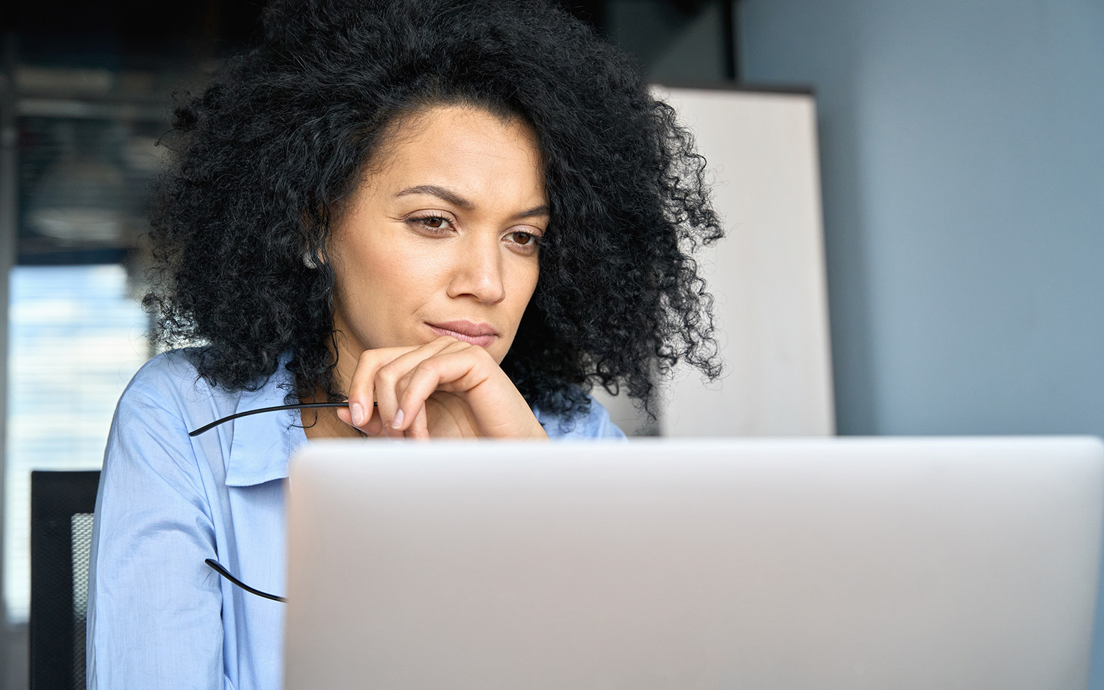 Young serious concerned businessperson sitting at desk looking laptop