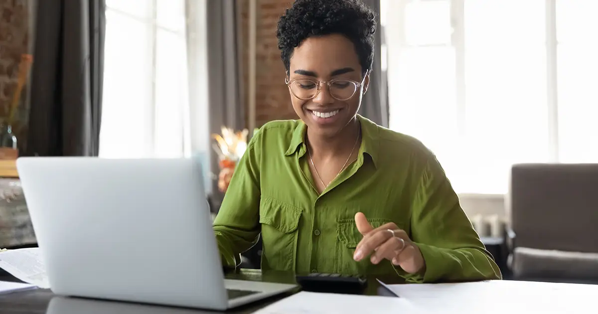 Happy young woman counting profit on calculator at laptop computer
