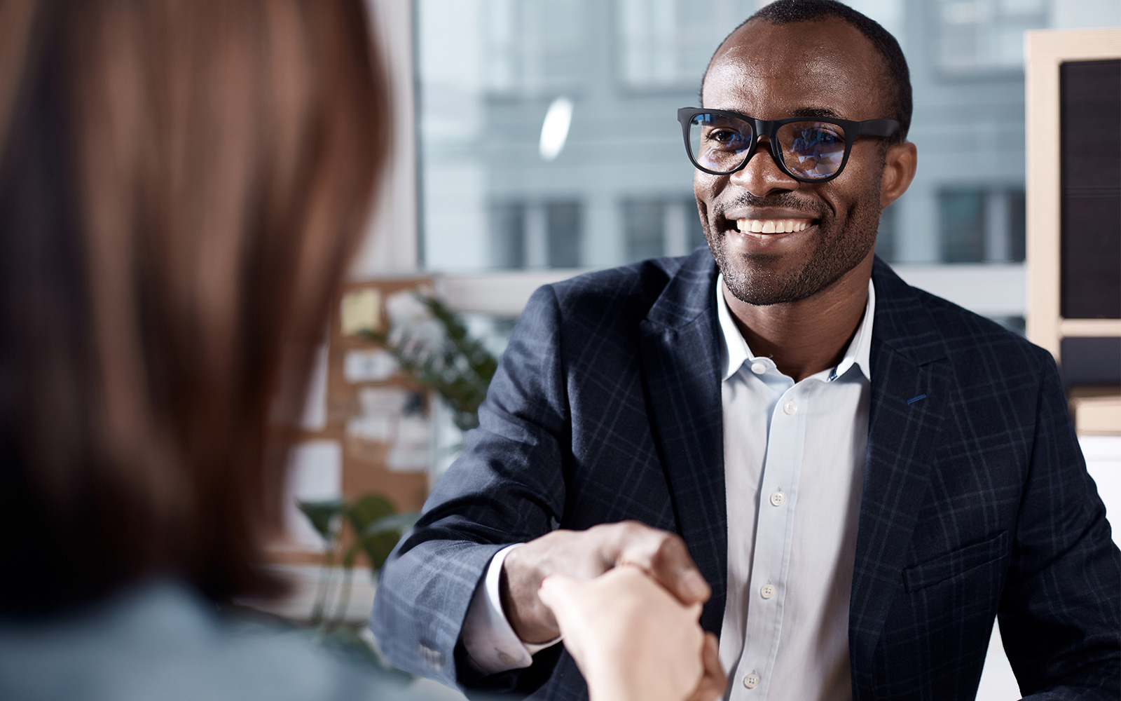 Manager in glasses is sitting at table and having firm handshake with Client