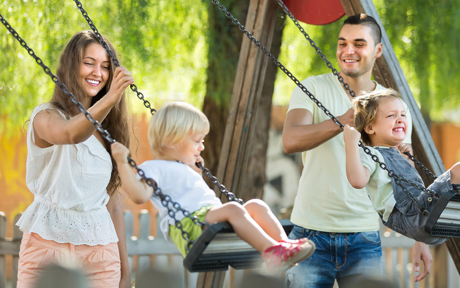 Happy young joyful family of four at playground swings