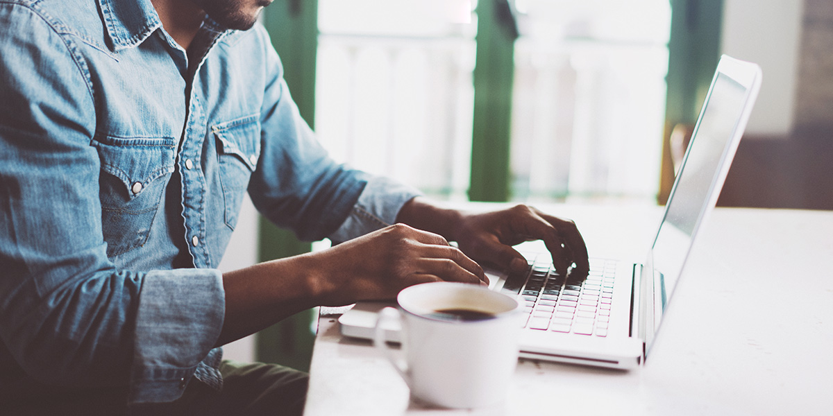 Person typing on a white laptop with a cup of coffee next to it.