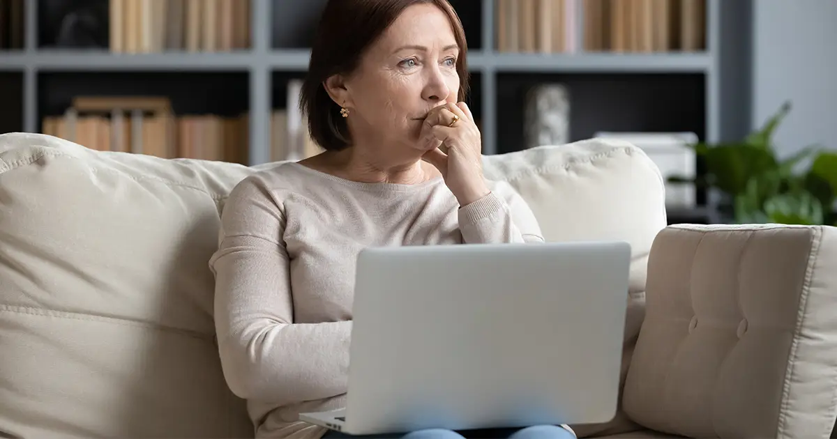 woman sit on couch in living room using laptop look in distance thinking or pondering