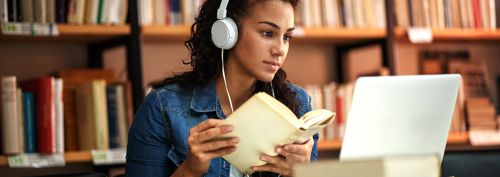 Student in the library using books and laptop