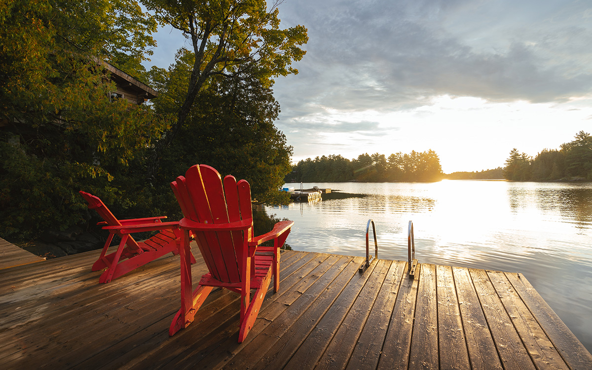Two Adirondack chairs on a dock facing the sunset.