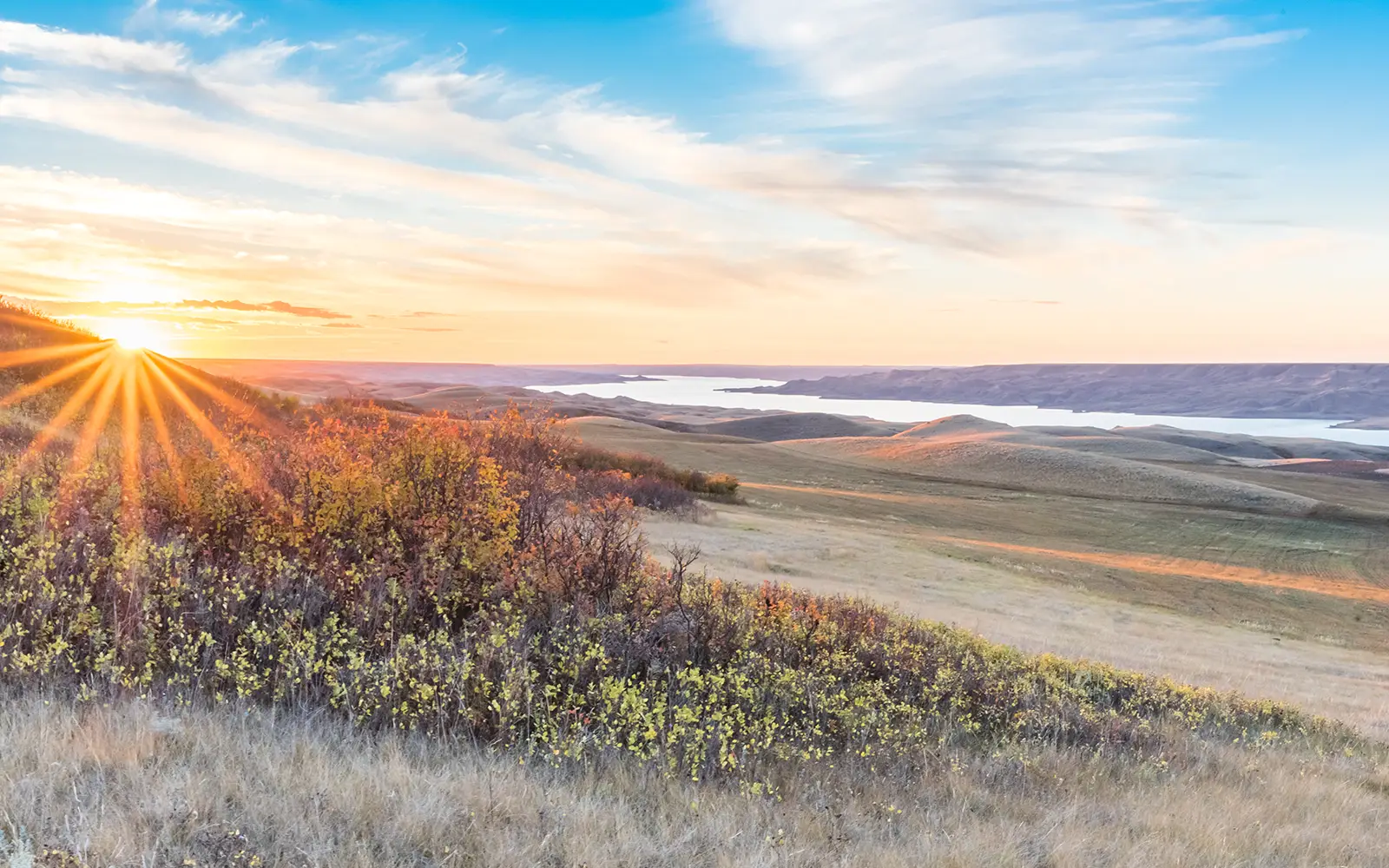 Sunrise over a field and valley with water running through it