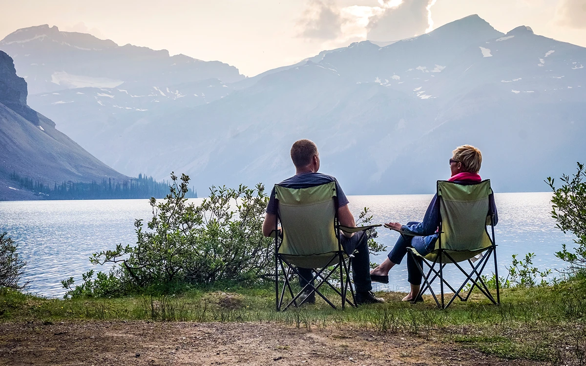 A couple sitting on camping chairs looking out at a lake in Alberta.