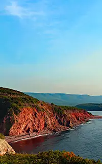 Red coastal cliffs meeting the ocean under a clear blue sky