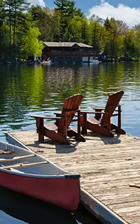 Two Adirondack chairs on a wooden dock overlook the tranquil blue waters of a Muskoka lake