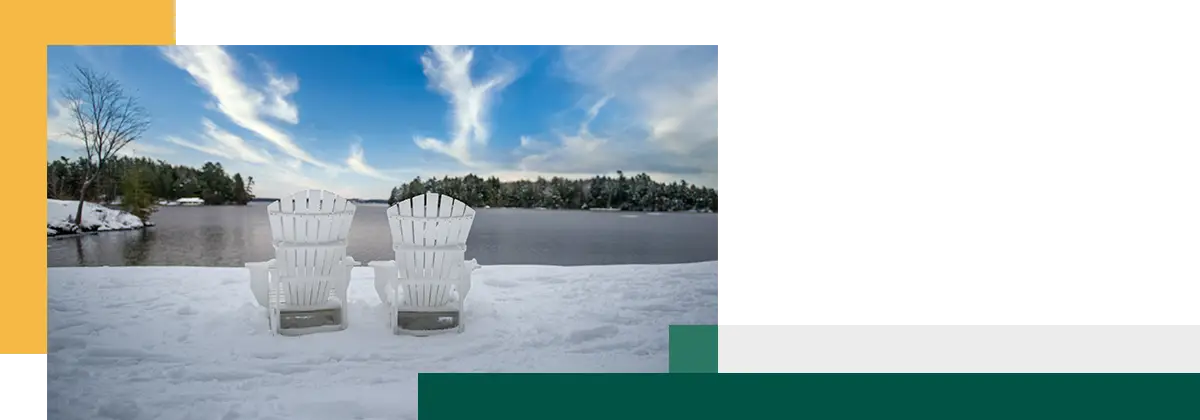 Two Adirondack chairs placed in front of a frozen lake.