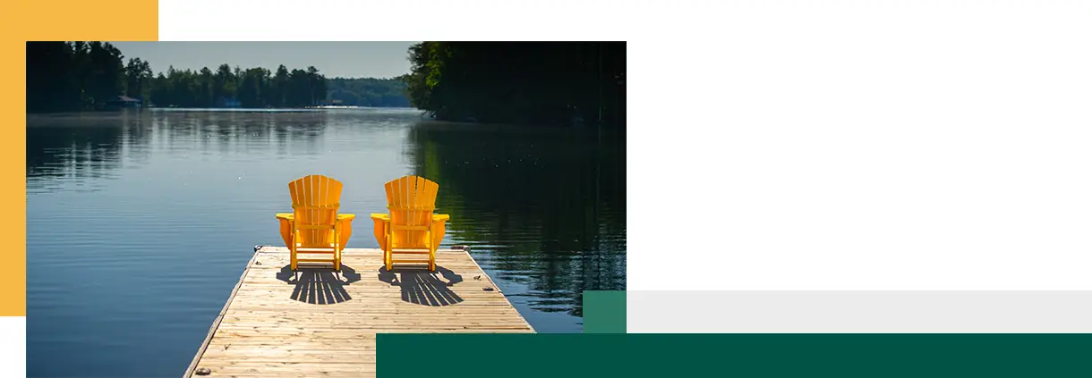 Rear view of two bright yellow Adirondack chairs on a wooden dock at sunrise in Muskoka, Ontario