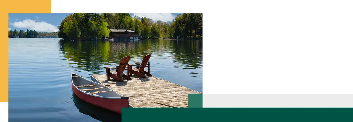 Two Adirondack chairs on a wooden dock overlook the tranquil blue waters of a Muskoka lake