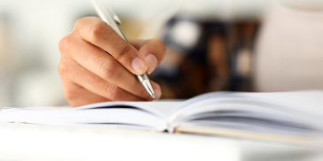 A person diligently writing in a book using a pen.