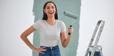 A woman smiles while holding a paint roller, ready to start her painting project with enthusiasm and joy.