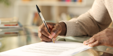 A person is signing a contract at a desk, demonstrating a formal business agreement.