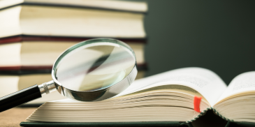 A magnifying glass rests on an open book, surrounded by a stack of books, symbolizing detailed study and glossary exploration.