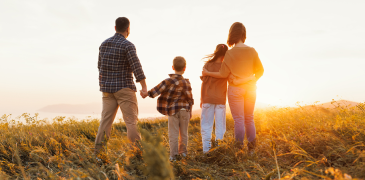 A family enjoys a serene moment in a field at sunset, with the sun casting a golden glow around them.