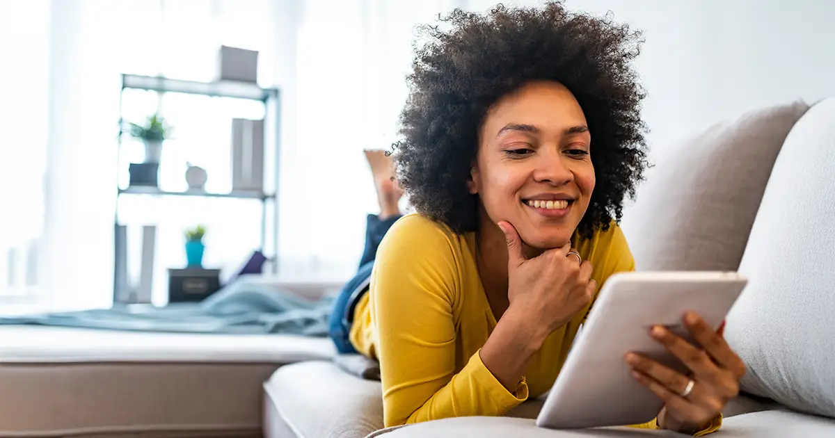 Happy young woman with tablet pc laying on sofa