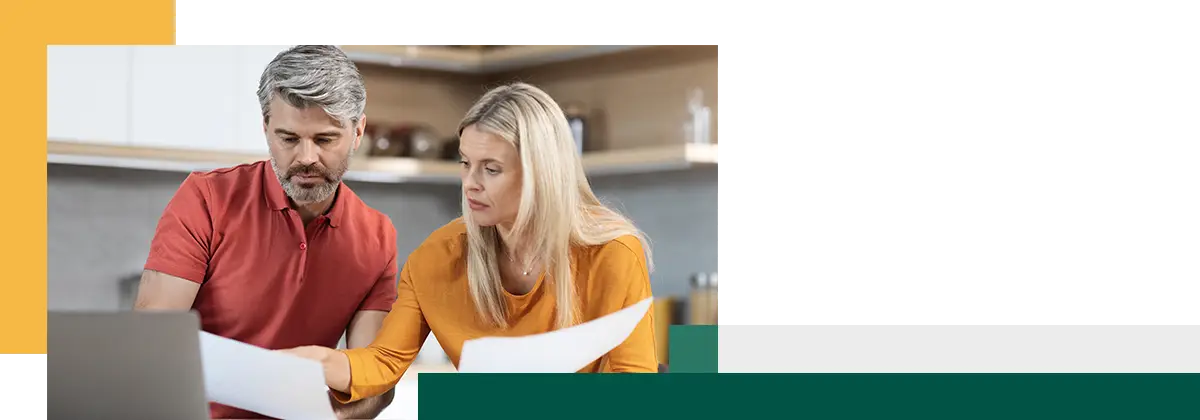 Middle aged husband and wife sitting at table in front of computer