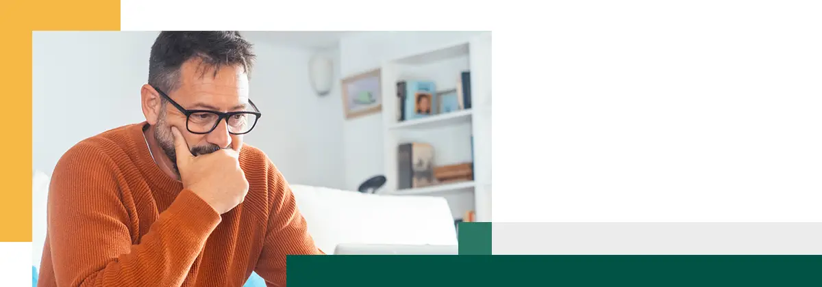 One thoughtful adult man in front of an open laptop thinking