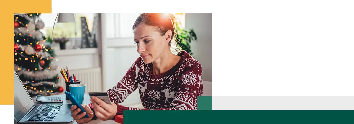 Woman wearing a patterned sweater sits at a table holding a credit card and a mug, with a small gift box in front of her.