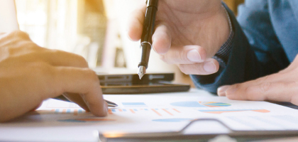 Two people's hands on documents. One person is holding a pen.