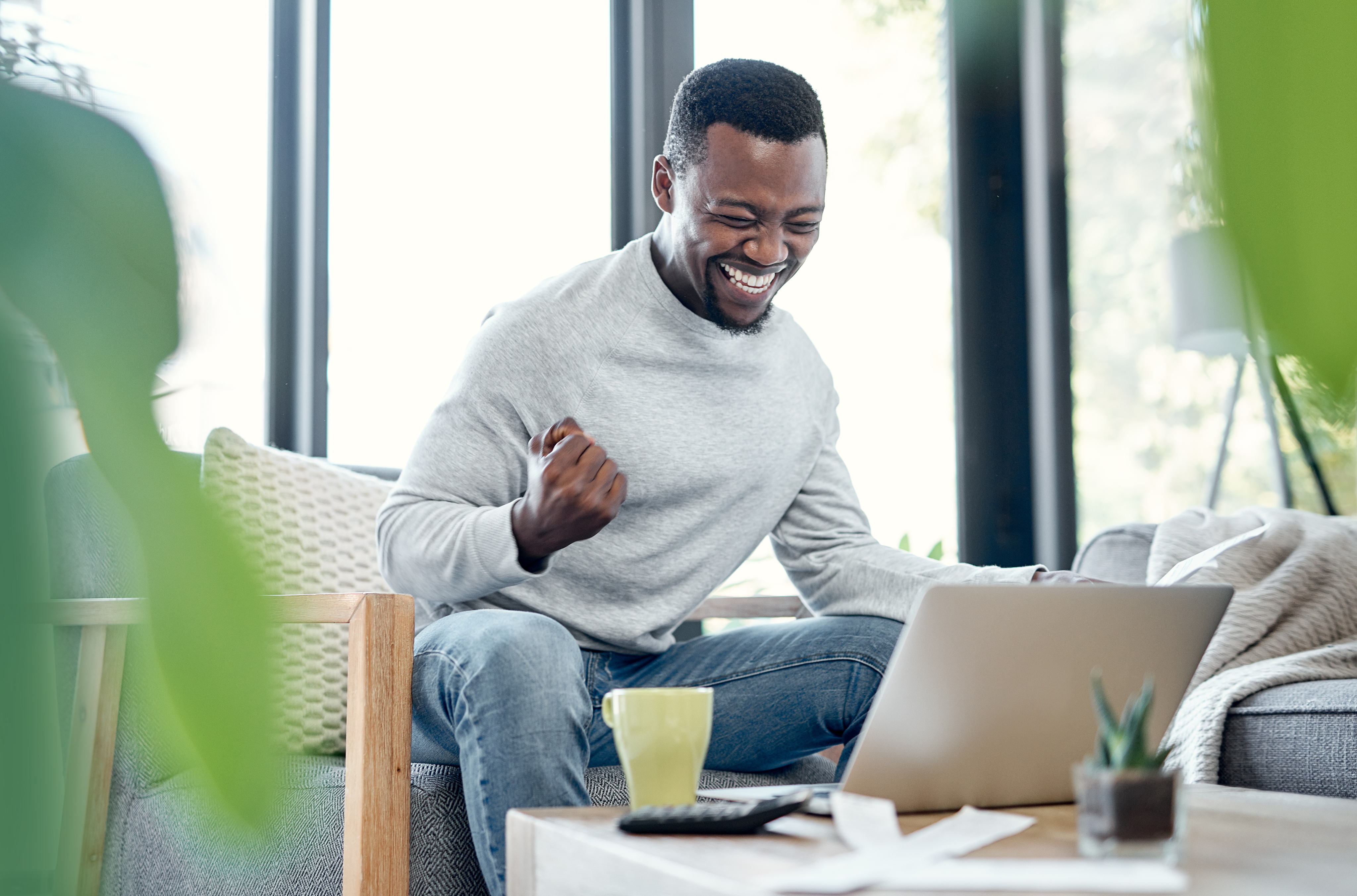 Man smiling at his laptop, raising a celebratory fist after becoming debt-free.