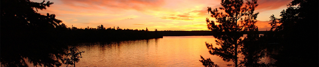 Small body of water silhouetted by a bright orange sunset.