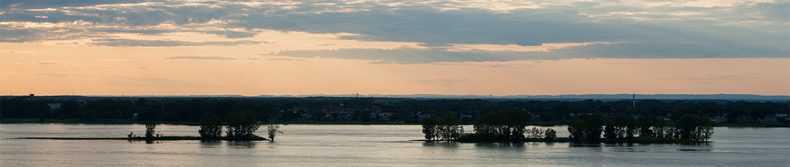 Body of water with small islands in the middle silhouetted by a rose morning sky